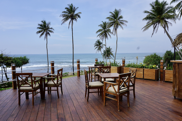 En bild på stolar och bord med utsikt över en tropisk strand och hav.