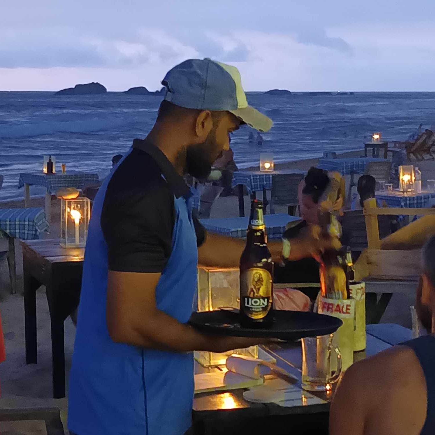 En närbild på en person som serverar öl i en strandbar i skymningen. Havet i bakgrunden.