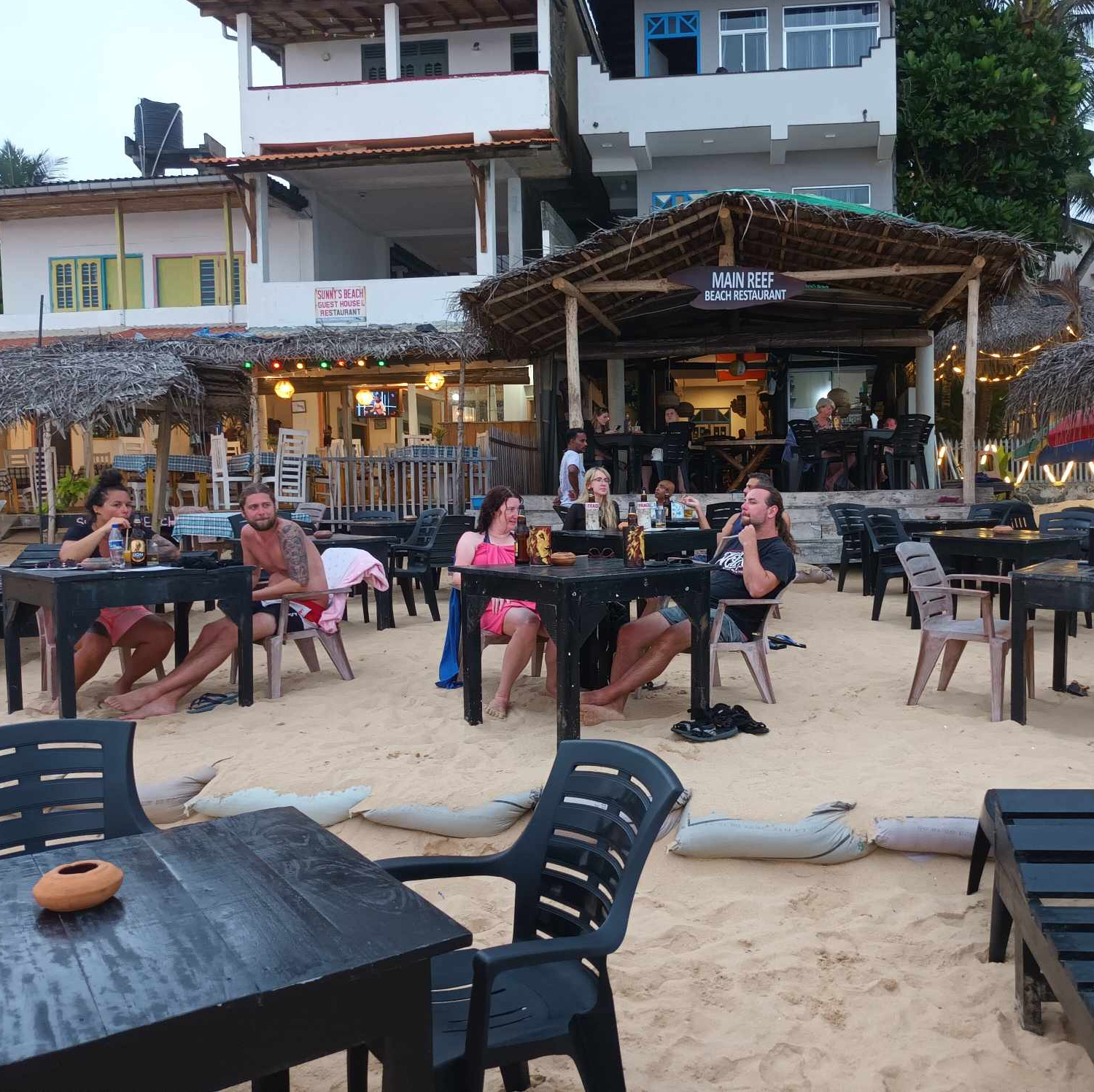En bild på restauranger på stranden med gord och gäster som sitter framför.