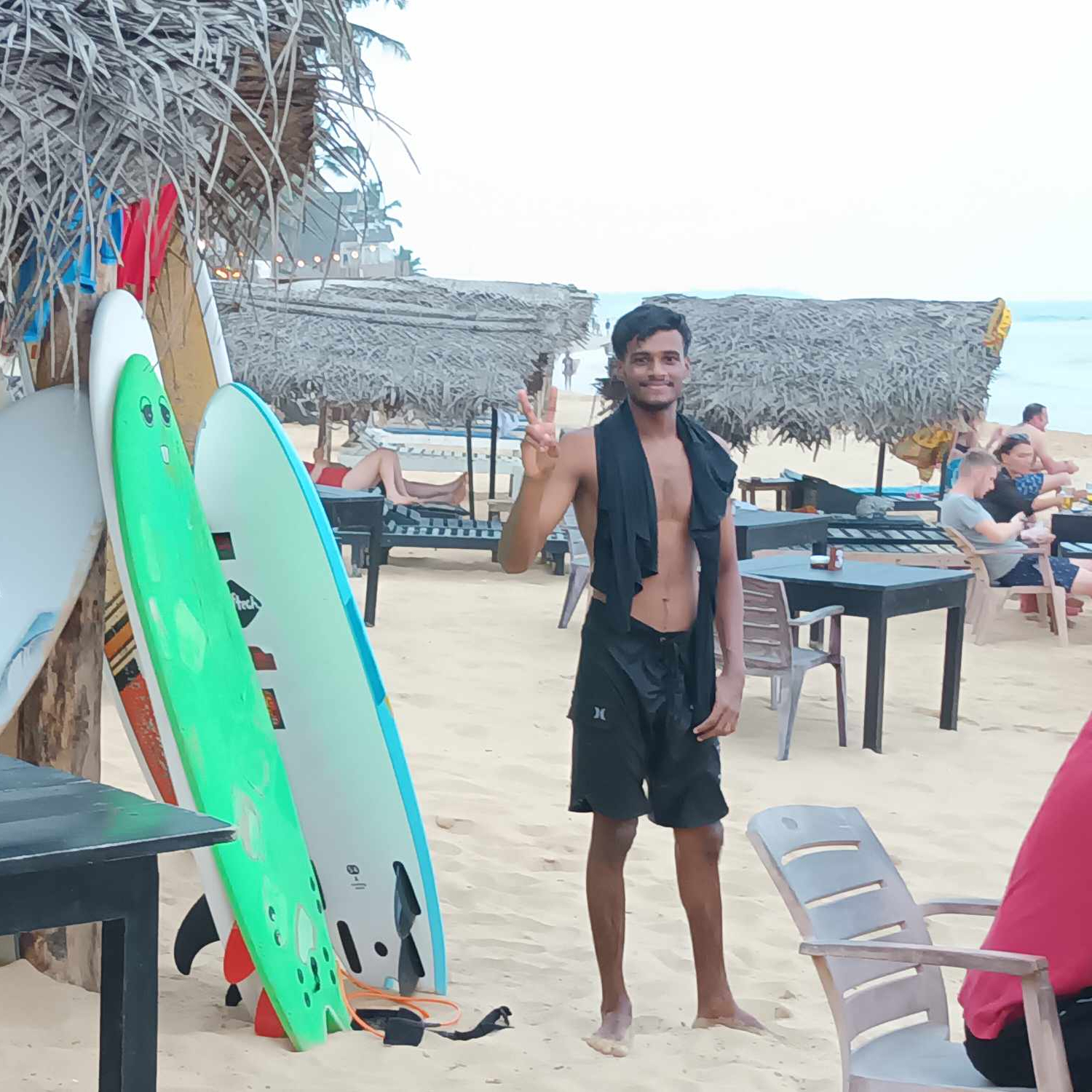 En bild på surfbrädor uppställda på stranden och en ung man i badbyxor.