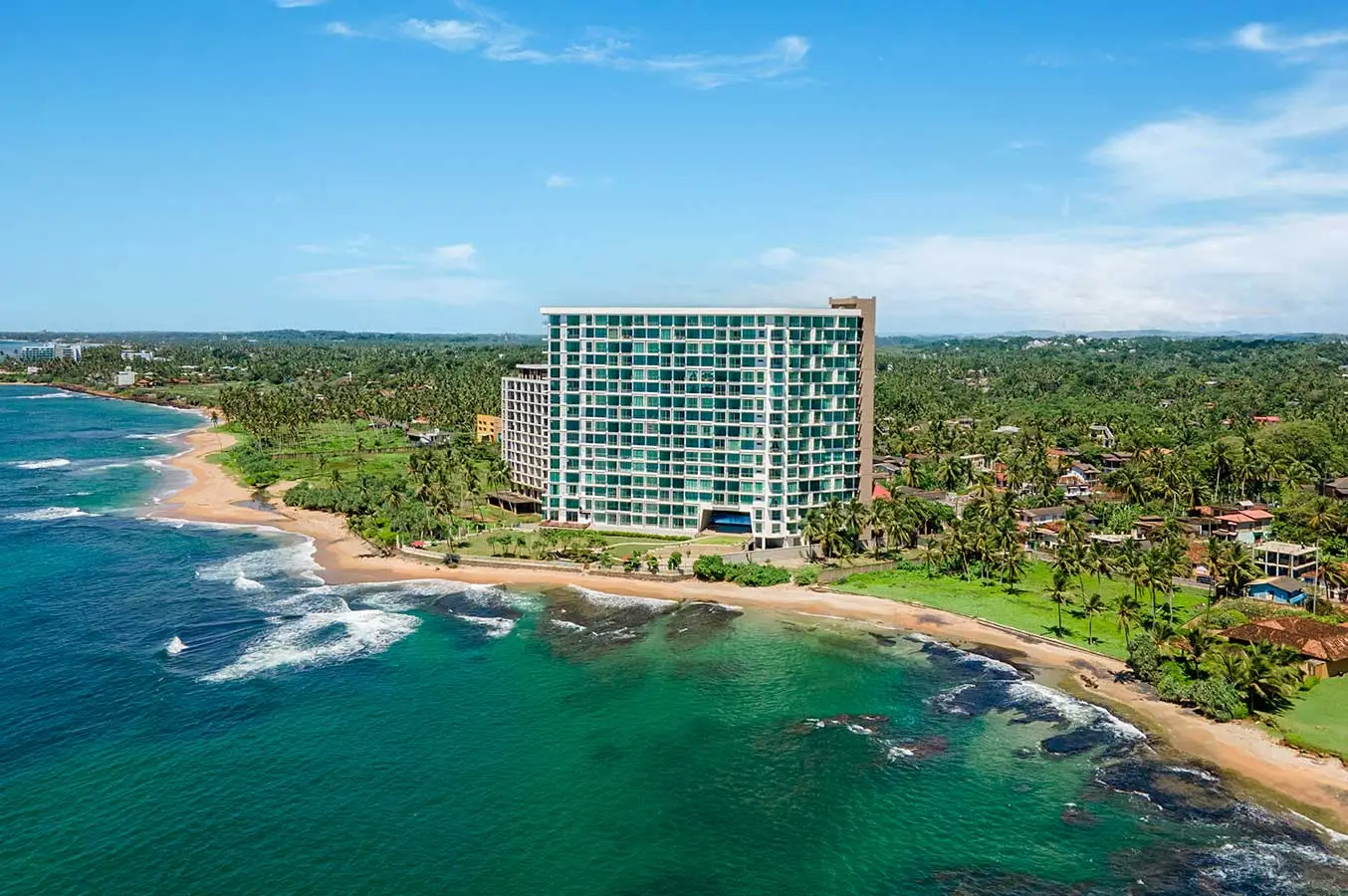 En bild på ett högt och lyxigt lägenhetshotell vid en tropisk strand, omgivet av palmer